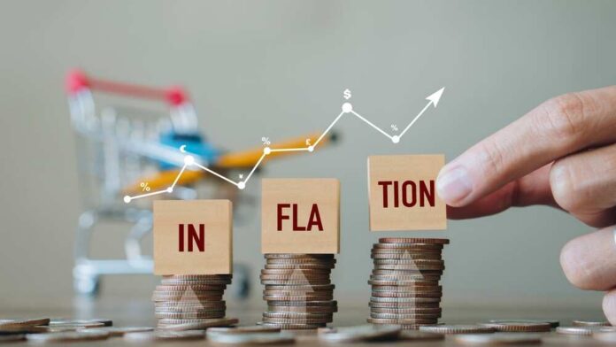 Hand pointing at blocks spelling 'INFLATION' on stacked coins with a shopping cart in the background