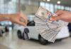 Hands exchanging car keys and a bundle of cash in a dealership