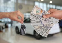 Hands exchanging car keys and a bundle of cash in a dealership