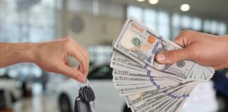 Hands exchanging car keys and a bundle of cash in a dealership