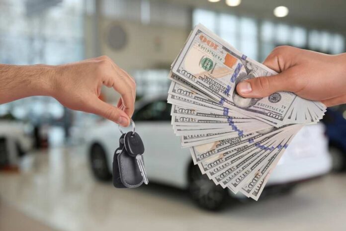 Hands exchanging car keys and a bundle of cash in a dealership