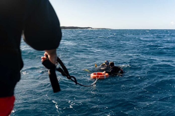 Crewman,Assisting,Scuba,Divers,Returning,To,Boat,With,Lifebuoy,After Two scuba divers in the ocean being assisted by a person holding a rescue line