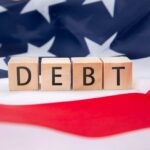Wooden blocks spelling 'DEBT' on an American flag background