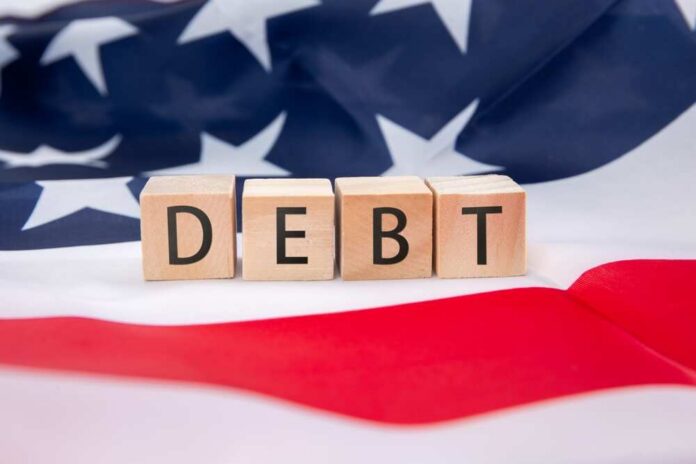 Wooden blocks spelling 'DEBT' on an American flag background