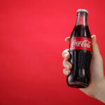 Coca-Cola Shutters Century-Old Facility Red sign with a white cross symbol on a dark background