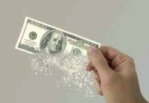 Hand holding a disintegrating hundred dollar bill.