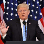 Trump Torches Netanyahu — ‘Crazy’ A man giving a speech with American flags behind.