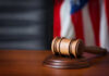 A wooden gavel resting on a sound block with an American flag in the background
