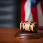 A wooden gavel resting on a sound block with an American flag in the background