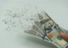 Iran War Drains $1,000 Fast Hundred-dollar bills disintegrating in hand.
