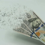 Iran War Drains $1,000 Fast Hundred-dollar bills disintegrating in hand.