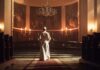 A religious figure standing in a church with candlelight illuminating the space