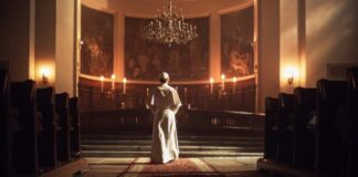 A religious figure standing in a church with candlelight illuminating the space