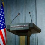 Trump Installs New Spy Chief Press podium with the White House sign and an American flag in the background