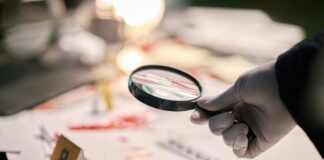 Gloved hand holding a magnifying glass over scattered forensic documents