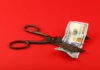 Hotel Jobs PLUNGE — Council Backtracks Scissors cutting a hundred dollar bill on a red background