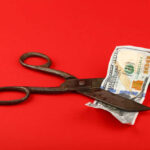 Hotel Jobs PLUNGE — Council Backtracks Scissors cutting a hundred dollar bill on a red background