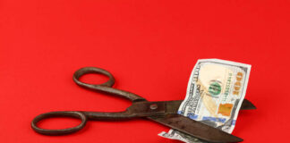 Scissors cutting a hundred dollar bill on a red background