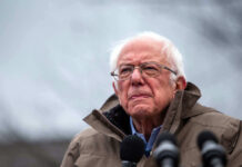 Bernie Sanders Targets THESE Billions?! Bernie Sanders wearing glasses speaking outdoors with microphones.
