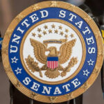 United States Senate seal with microphones in front.