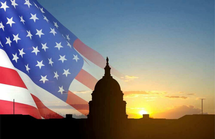 shutterstock_23679936071 U.S. Capitol silhouette with American flag and sunrise.