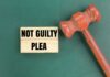 A wooden gavel next to a sign that reads 'NOT GUILTY PLEA'