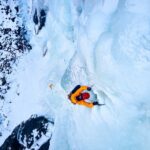A climber ascending a frozen ice wall in a snowy landscape