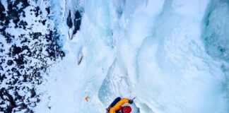 A climber ascending a frozen ice wall in a snowy landscape
