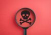 City Towers Spray — Five Dead Magnifying glass focusing on a skull and crossbones symbol against a red background