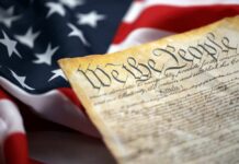 Close-up of a historical document with the American flag in the background