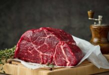 Beef Drops, Chaos Erupts Over Why A raw cut of beef on a wooden board with herbs and a pepper grinder