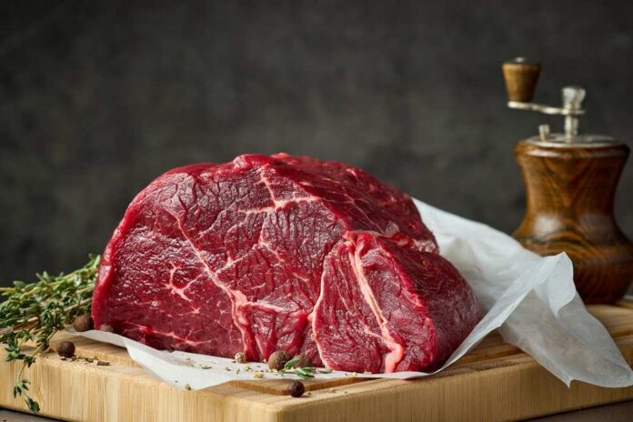 Fresh,Raw,Beef,Meat,With,Herbs,And,Spices,On,Wooden A raw cut of beef on a wooden board with herbs and a pepper grinder