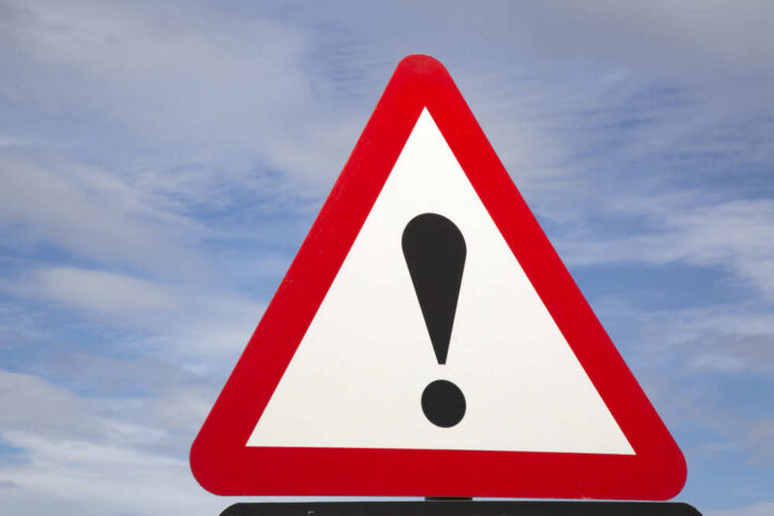 Warning road sign with exclamation mark against a cloudy sky
