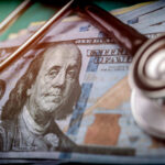 A stethoscope resting on a stack of hundred-dollar bills