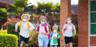 Children with backpacks and masks running outside school.