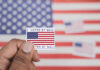 Hand holding a vote-by-mail sticker with U.S. flag