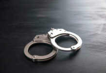 Chilling Mask, Dozen Victims — Then Arrest Metal handcuffs on a dark textured surface.