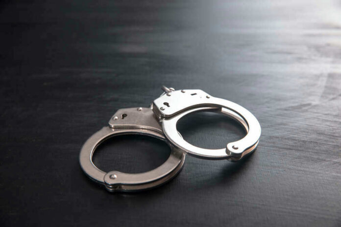 shutterstock_1857504991 Metal handcuffs on a dark textured surface.