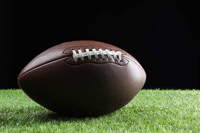 Leather,American,Football,Ball,On,Green,Grass,Against,Black,Background Football player kneeling on the field with a helmet beside them