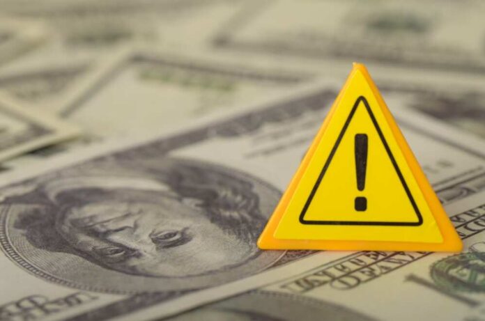 The,Yellow,Warning,Sign,Superimposed,On,Us,Dollar,Bills,Warns A yellow warning sign placed on a background of dollar bills