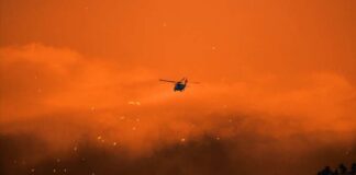 Helicopter fighting massive forest fire with water bucket.