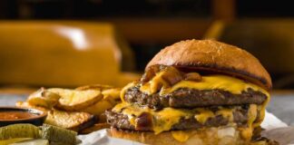 A double cheeseburger with melted cheese and pickles served with potato wedges