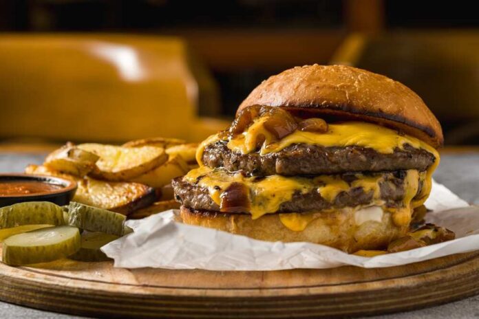 Smash,Burger,With,Cheddar,Cheese,And,Caramelized,Onions,,Served,With A double cheeseburger with melted cheese and pickles served with potato wedges