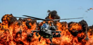 Military Apache helicopter flying through a cloud of smoke