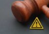Wooden gavel with a yellow warning triangle sign on dark surface