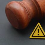 Wooden gavel with a yellow warning triangle sign on dark surface
