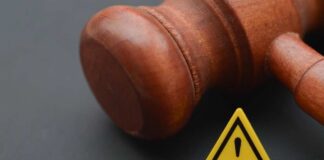 Wooden gavel with a yellow warning triangle sign on dark surface