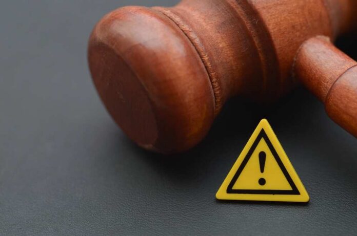 Judge's,Gavel,Is,Juxtaposed,With,A,Yellow,Caution,Sign,Featuring Wooden gavel with a yellow warning triangle sign on dark surface
