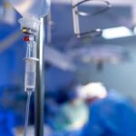 IV drip in focus with surgeons operating in the background