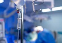 IV drip in focus with surgeons operating in the background